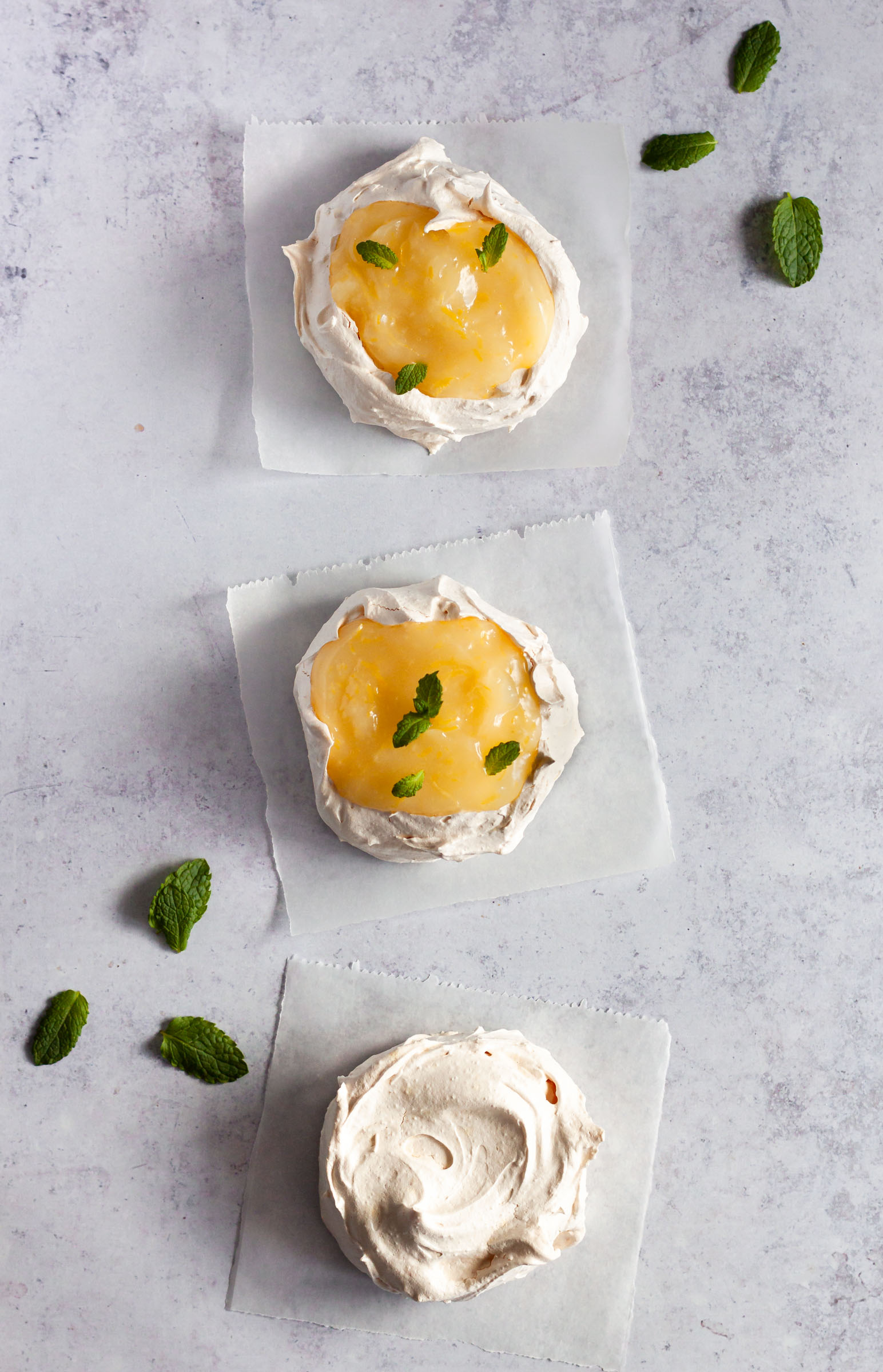 Three mini meringues decorated with lemon curd and fresh mint.