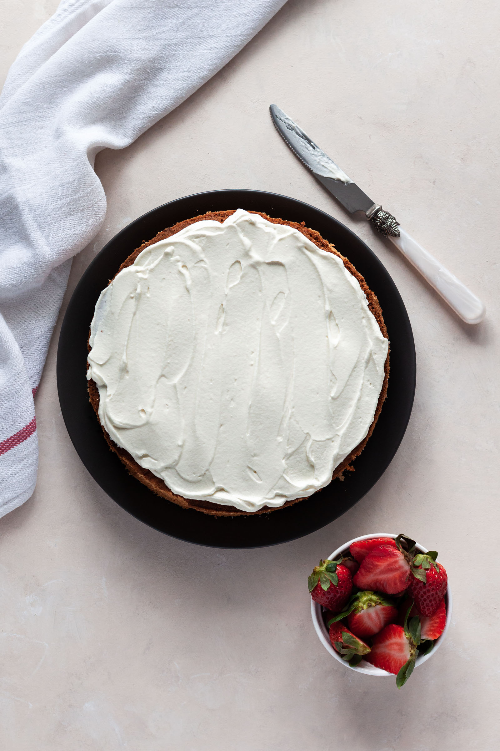 Sponge cake decorated with mascarpone cream,with fresh strawberries and a knife on the side.