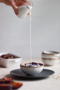 Pouring milk over a bowl of baked porridge