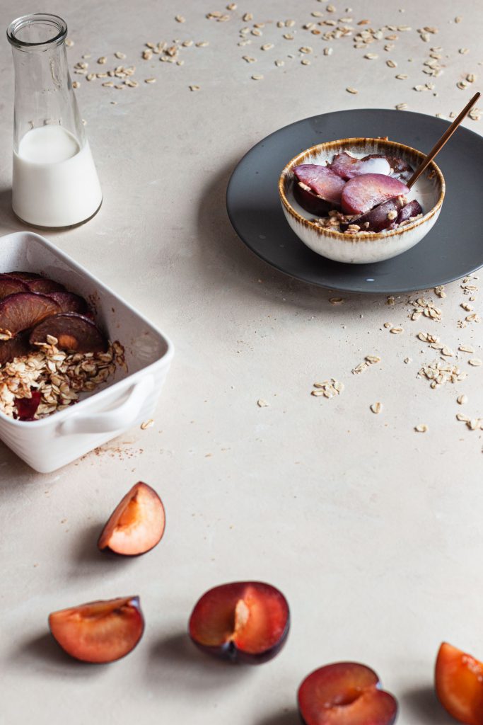 Baked oatmeal in a breakfast bowl with milk and fresh plum on the side.