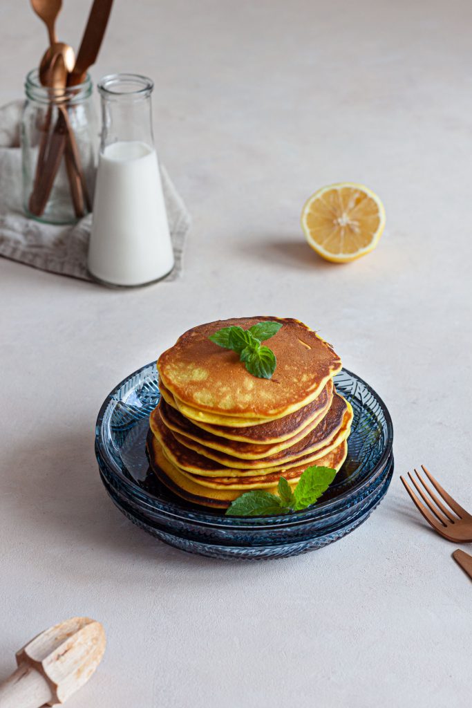 A stack of lemon goat cheese pancakes on a plate, topped with fresh mint leaves.