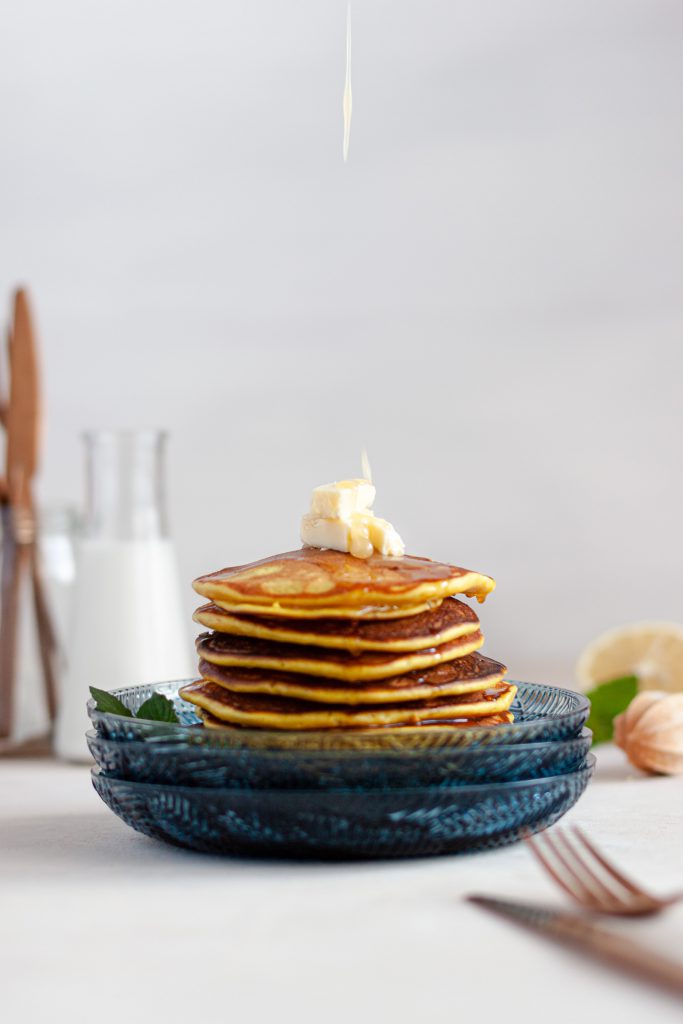 Pouring honey on a stack of lemon goat cheese pancakes topped with butter.