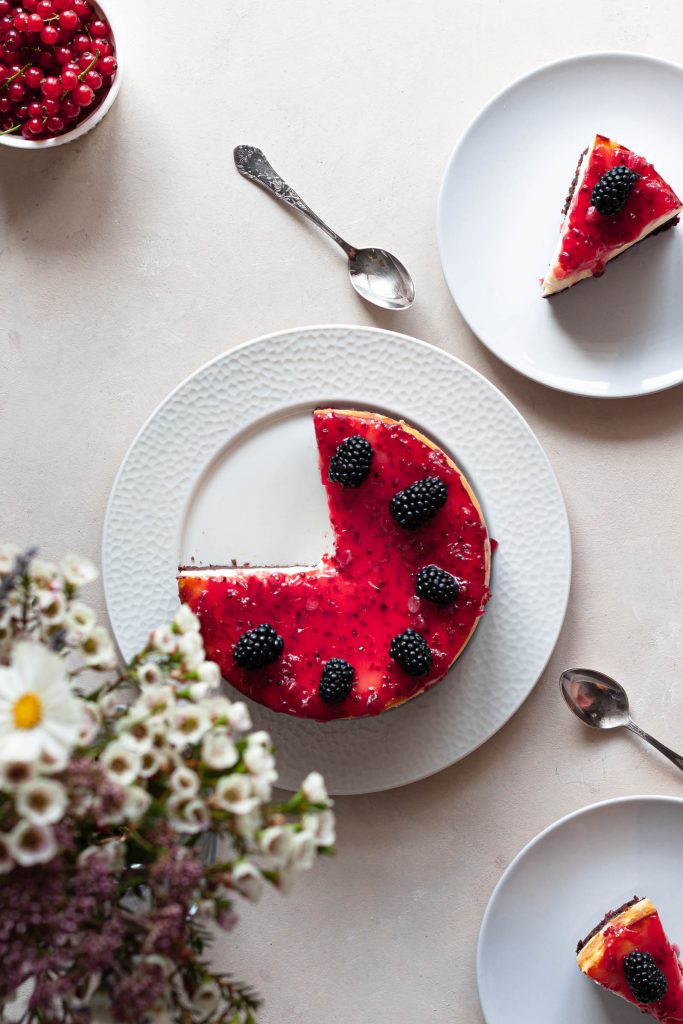 A tablescape of cheesecake with two slices taken out, served on two plates next to it.