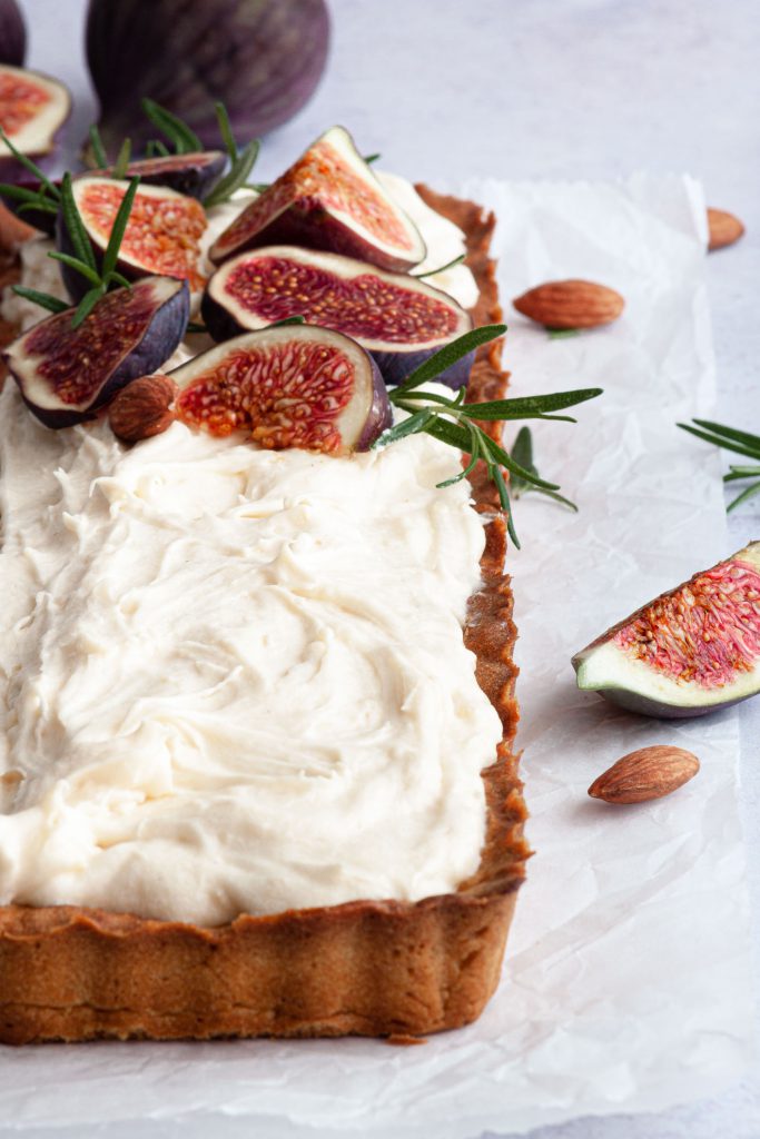 Crispy tart with a layer of almond cream frosting decorated with slices of fresh figs, almonds and rosemary.