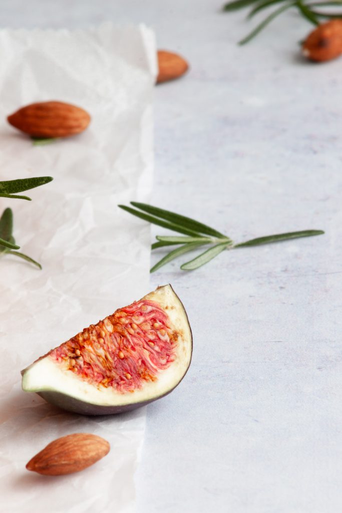 A slice of fig tart with almonds and rosemary pieces around it.
