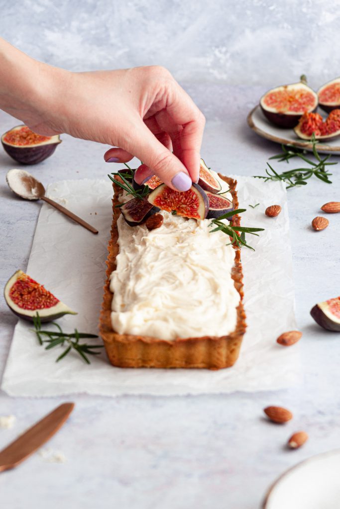 A hand decorating tart with fresh figs with a plate of fresh figs in the background.