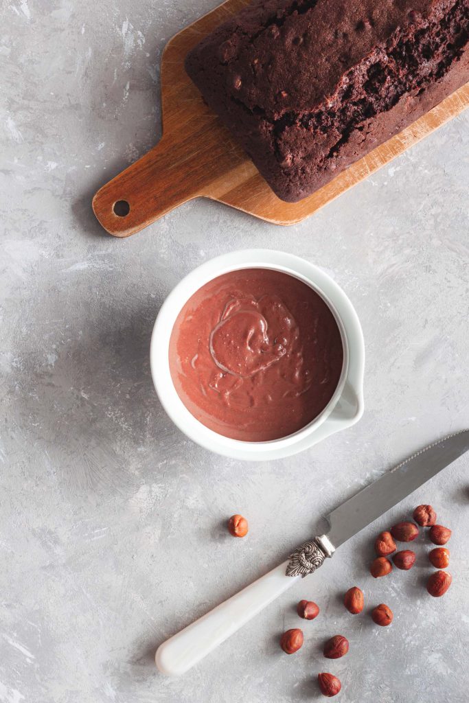 An overhead photo of chocolate ganache in a serving bowl and chocolate cake on a chopping board.