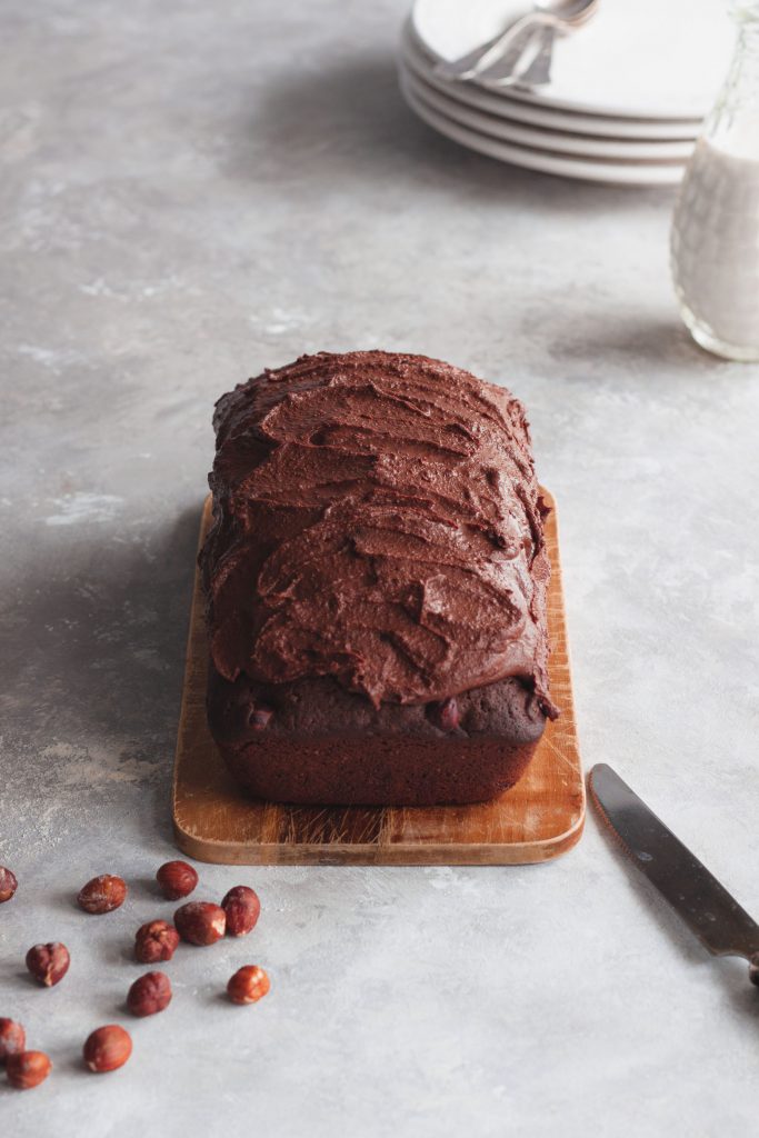 Chocolate cake decorated with ganache, hazelnuts and knife on the side.