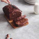 Hand slicing chocolate cake decorated with chocolate ganache.