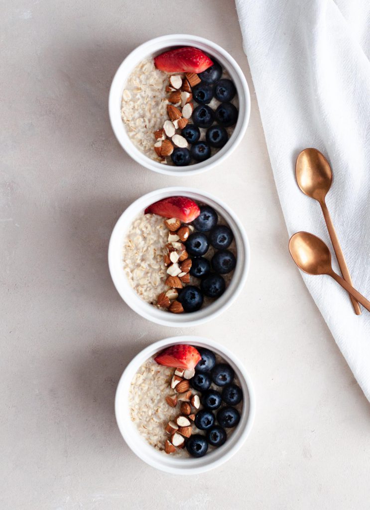Coconut milk oatmeal served in breakfast bowls, decorated with fresh fruit and almonds.