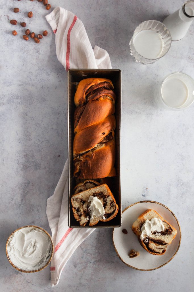Baked babka in a loaf tin, a few slices on the side served with cream cheese.