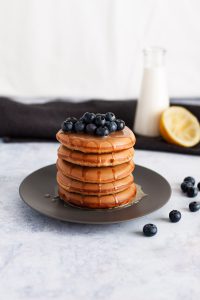 A stack of pancakes topped with fresh blueberries and honey.