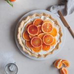 Tart topped with mascarpone cream and tangerines, a knife and slices of tangerines on the side.