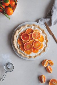 Tart topped with mascarpone cream and tangerines, a knife and slices of tangerines on the side.