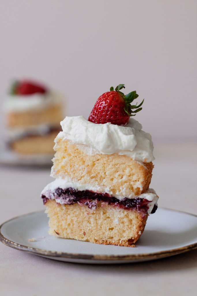 A slice of the cake topped with a strawberry, with layers of cake, preserve and whipped cream visible.